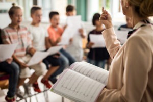 Barn övar körsång. Unrecognizable teacher giving a lesson during music class.